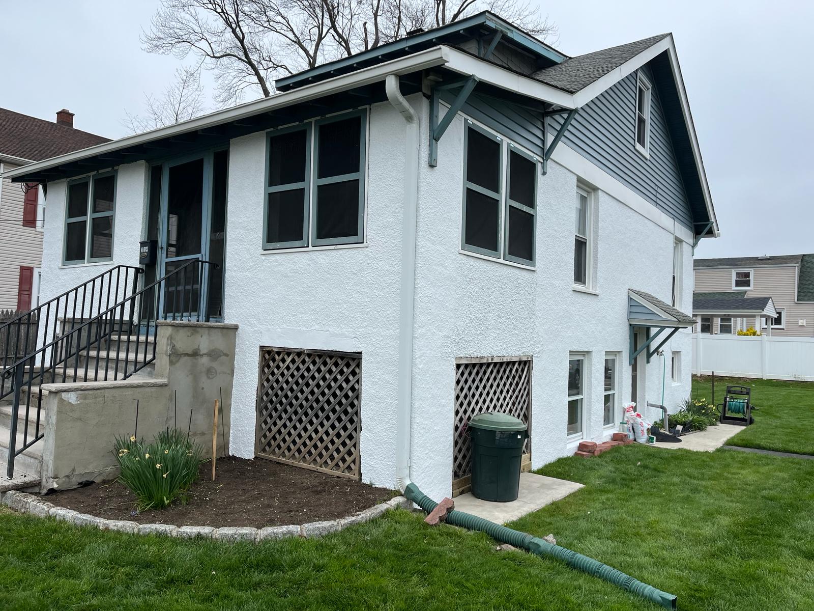 Two-story stucco home exterior painted white with deep green trim