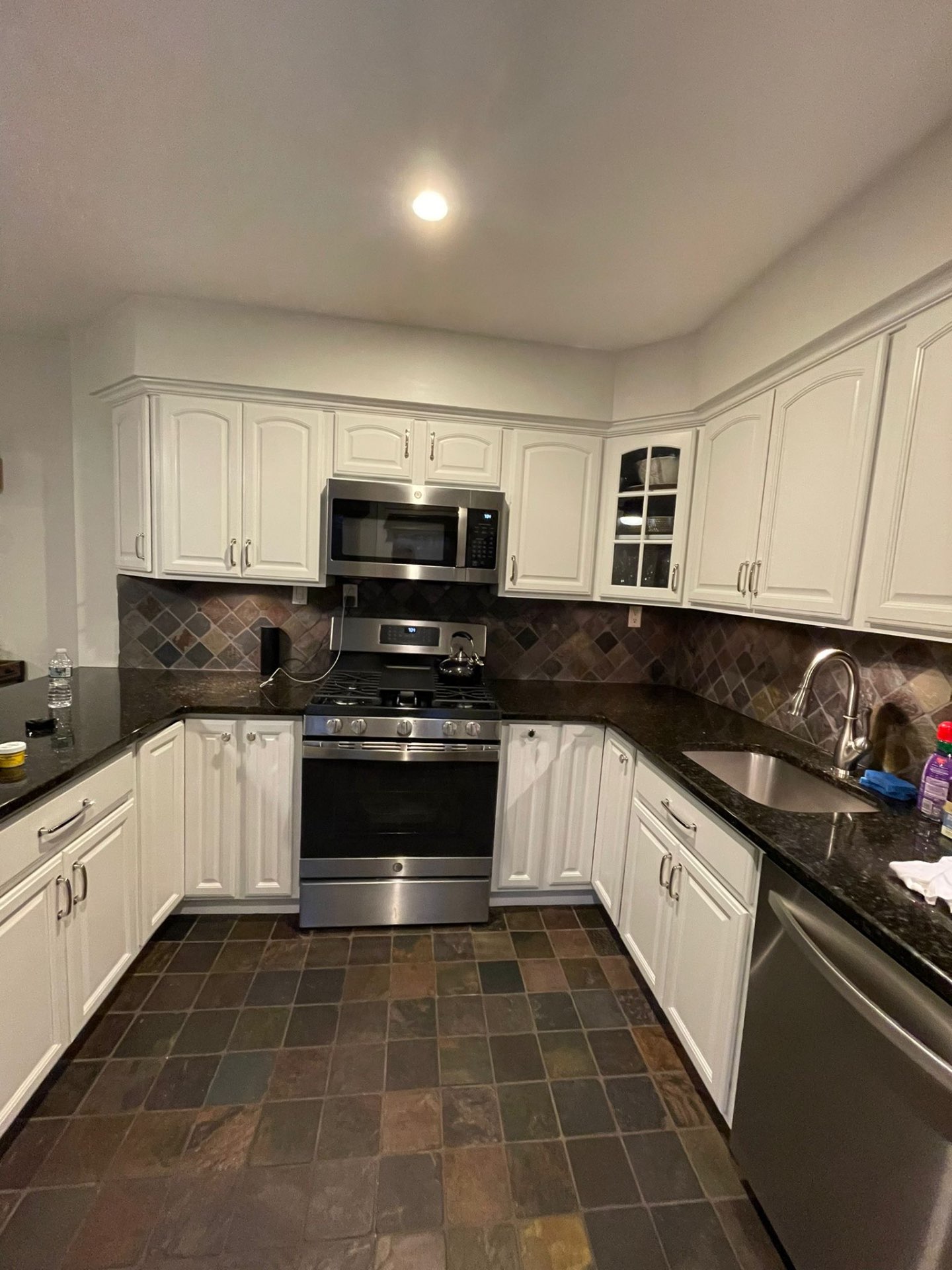 Kitchen with arched cabinet doors repainted white above slate flooring